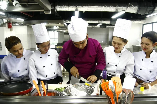Szef kuchni uczy studentów kulinarne jak prawidłowo cut świeże warzywa w klasie gotowania. — Zdjęcie stockowe