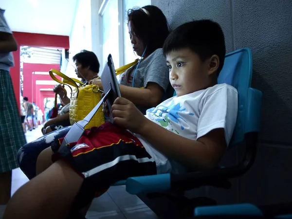 Un niño juega un videojuego en una tableta mientras está en una sala de espera de una clase de matemáticas . — Foto de Stock