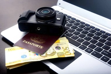Kamera, pasaport ve Filipin Pezosu faturaları bir dizüstü bilgisayar üzerinde.