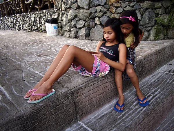 Young girls play a video game on a smartphone while sitting on a set of steps. — Stock Photo, Image
