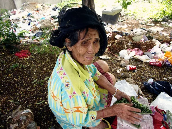 老婦人は狩りまたは放棄された多くのゴミの山でリサイクル可能な材料の清掃. — ストック写真