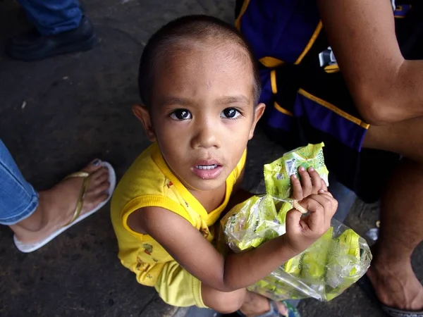 Chlapec se dívá na kameru, jak drží balíčky nezdravé potraviny nebo čipy, které se jí jako občerstvení na chodníku. — Stock fotografie