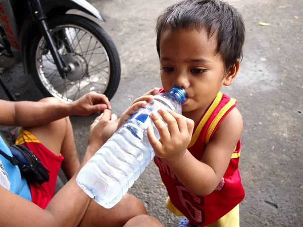 A boy drinks from a bottle while on a sidewalk. — Stock Photo, Image