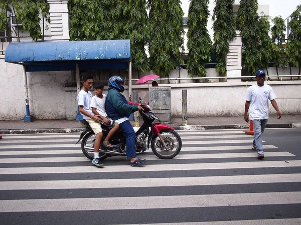 Ein Motorradfahrer mit zwei Insassen hält an, um einen Mann auf einem Fußweg passieren zu lassen. — Stockfoto