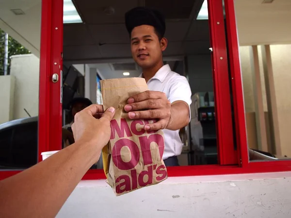 Un operaio di un fast food consegna un ordine di cibo a un cliente in un drive attraverso un bancone . — Foto Stock