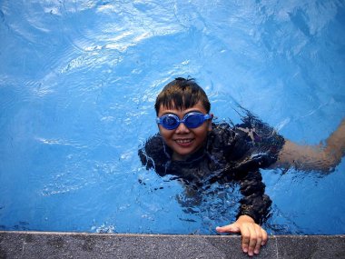 Young boy swimming and floating in a swimming pool clipart