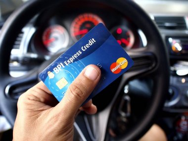 Bir otomobilin direksiyon önünde bir el tarafından düzenlenen BPI Expres kredi Mastercard.