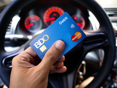 Bir otomobilin direksiyon önünde bir el tarafından düzenlenen bir Bdo banka kartı Mastercard.