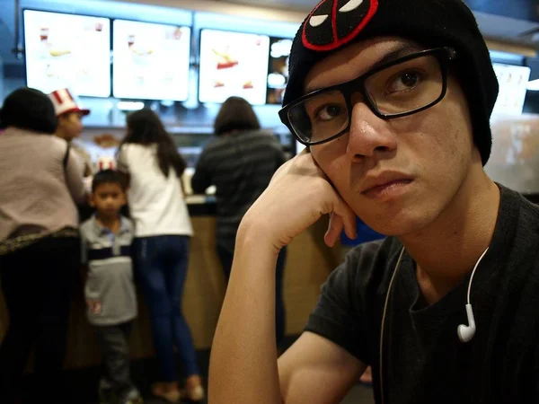 Um adolescente senta-se e espera por sua comida dentro de um restaurante de fast food em um shopping . — Fotografia de Stock