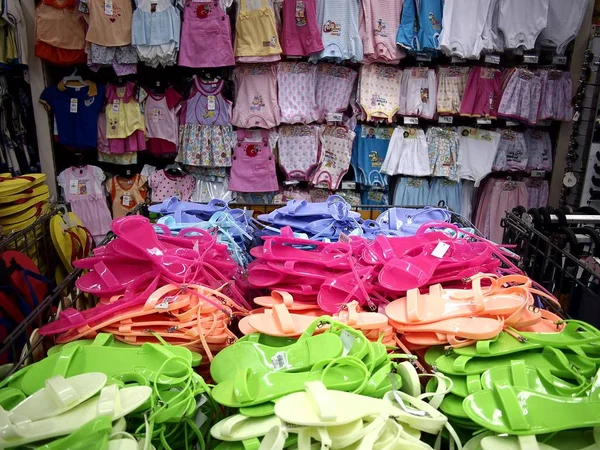 Pantofole di gomma colorata e vestiti assortiti in mostra in un negozio di alimentari . — Foto Stock