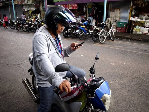 Cep telefonunu bir mesaj kontrol etmek için bir kaldırım bir motosiklet binici durur.