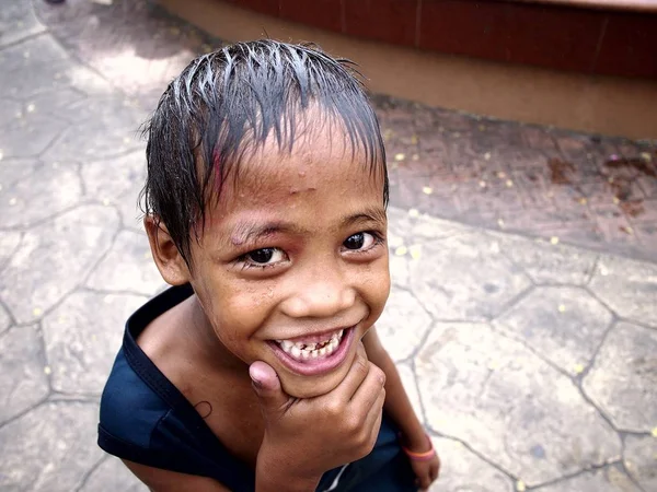 Un niño sonríe para la cámara después de mojarse en una fuente de agua en un parque al aire libre . — Foto de Stock