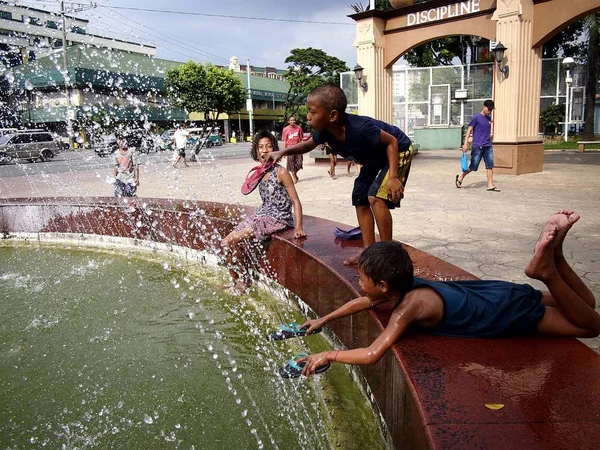 Les jeunes enfants jouent et se rafraîchissent dans une fontaine d'eau dans un parc extérieur . — Photo