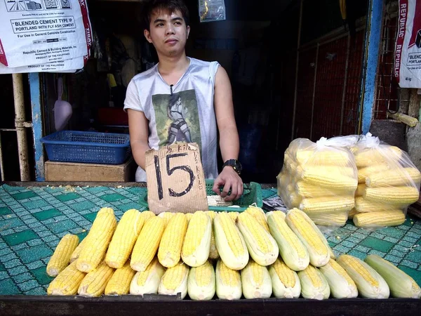 Um vendedor vende milho cru fresco numa loja num mercado público . — Fotografia de Stock