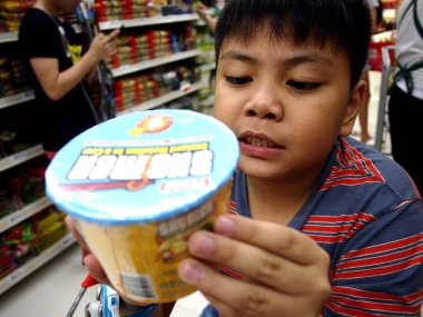 Genç bir çocuk bir anlık erişte Kupası bir bakkal etiketini okur.