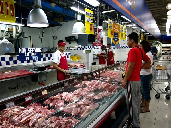 Un empleado de comestibles sirve productos cárnicos frescos a los clientes . — Foto de Stock