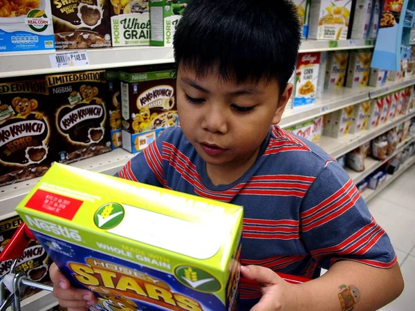 Genç bir çocuk bir bakkal bir Mısır gevreği kutusu etiketini okur. — Stok fotoğraf