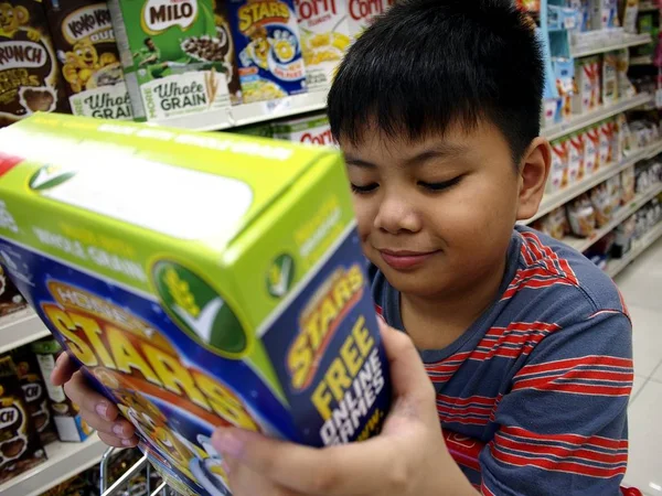 Un niño lee la etiqueta de una caja de cereales en una tienda de comestibles . — Foto de Stock