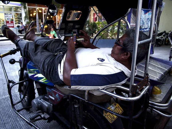 Un conductor se relaja en su triciclo y juega un videojuego en su smartphone . — Foto de Stock