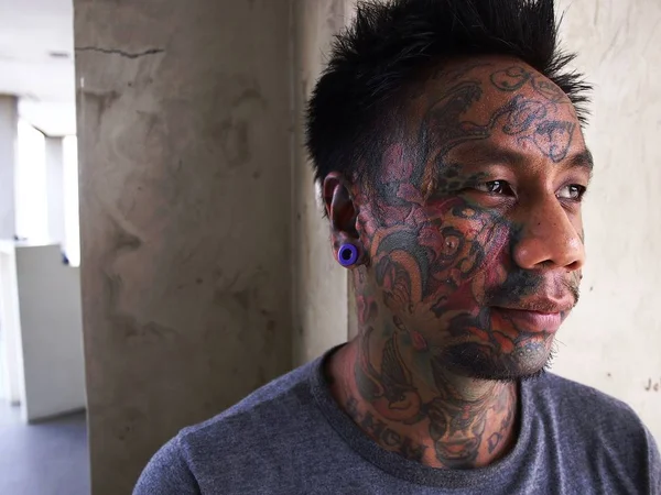 Un homme avec de l'art corporel montre son tatouage facial et son perçage d'oreille . — Photo