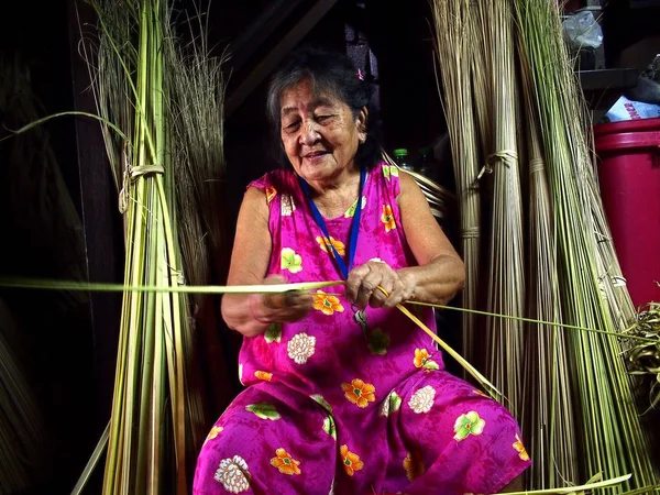 En äldre dam trimmar coconut tree löv att användas som emballage för en lokal delikatess kallas Suman eller kokt glupsk ris. — Stockfoto