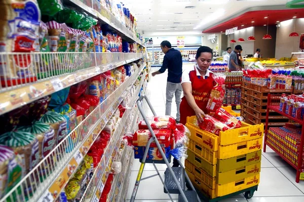 Un trabajador organiza diferentes tipos de pan en un expositor dentro de una tienda de comestibles . — Foto de Stock
