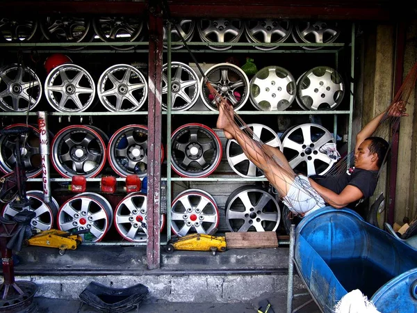 Un uomo riposa su un'amaca davanti al suo negozio di pneumatici per la cura . — Foto Stock