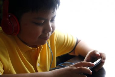 Bir akıllı telefon ve kulaklık ile genç Asyalı çocuk