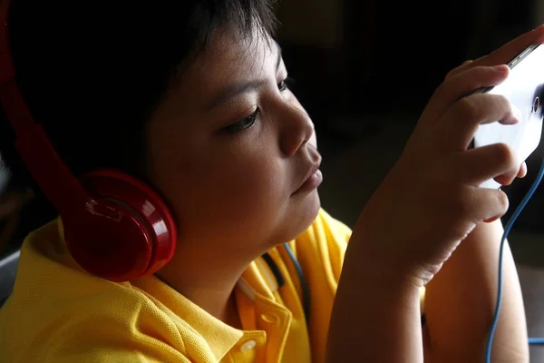 Jovem menino asiático com um smartphone e fones de ouvido — Fotografia de Stock