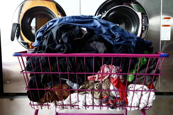 Manojo de ropa limpia en una cesta delante de las lavadoras — Foto de Stock