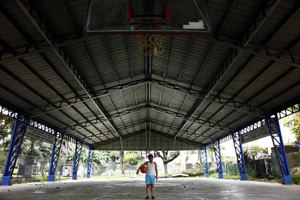 Young Filipino boy stands on the free throw line of a basketball court and holds a basketball. — Stock Photo, Image