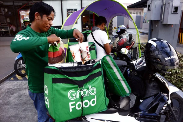 El conductor de una popular empresa de distribución de alimentos carga alimentos para un cliente a su motocicleta. —  Fotos de Stock