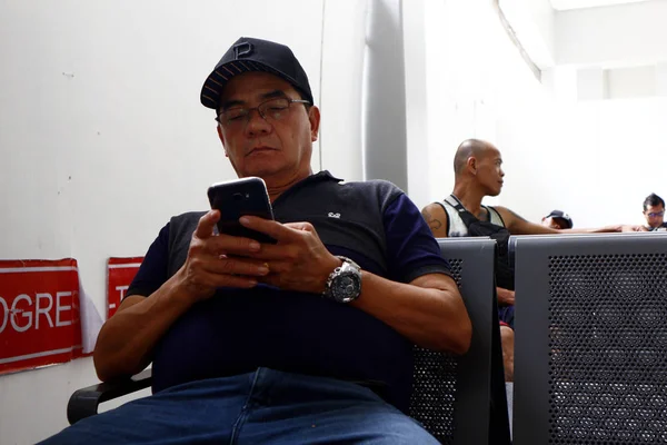 성인 필리핀 남자 는기다리고 있는 지역에서 시간을 보내기 위해 스마트폰을 사용 한다 — 스톡 사진