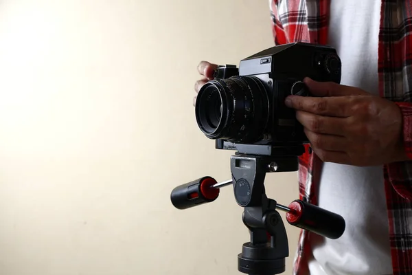 Homem adulto segurando uma câmera de filme de formato médio antigo e vintage em um tripé . — Fotografia de Stock