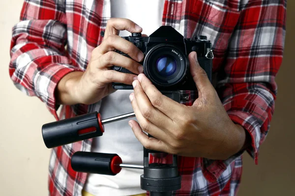 Adult man holding an old and vintage small format or 135mm film camera on a tripod — Stock Photo, Image