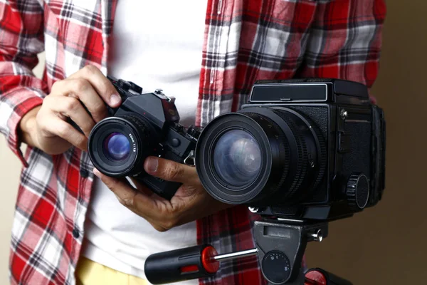 Чоловік тримає 35 мм плівкову камеру і стоїть за камерою середнього формату на тринозі — стокове фото
