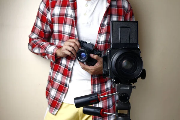 35mm 필름 카메라를 들고 삼각대 위에 중간 포맷 필름 카메라 뒤에 서 있는 남자 — 스톡 사진