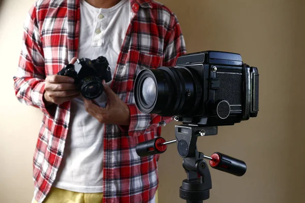 Hombre sosteniendo una cámara de película de 35 mm y de pie detrás de una cámara de película de formato medio en un trípode —  Fotos de Stock