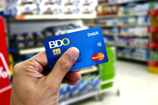 Hand hålla en bank debet- och bankomat kort medan inne i en stormarknad. — Stockfoto