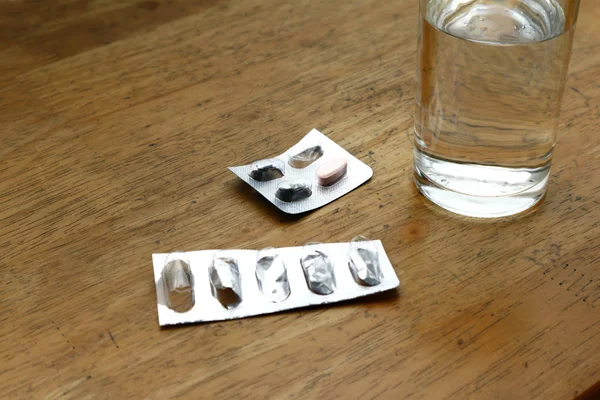 Пустая упаковка с лекарствами на столе и стакан воды — стоковое фото