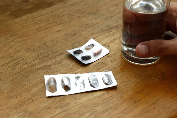 Emballages vides de papier d'aluminium de médecine sur une table et main tenant un verre d'eau — Photo