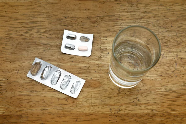 Emballages vides de papier d'aluminium de médecine sur une table et un verre d'eau — Photo