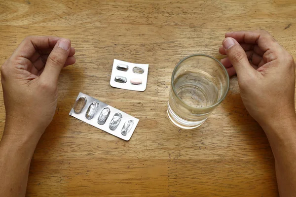 Embalajes de papel de medicina vacíos en una mesa, un vaso de agua y un par de manos —  Fotos de Stock