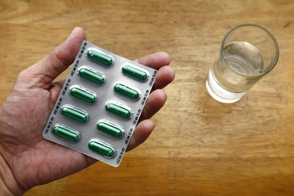 Mano sosteniendo un paquete de papel de aluminio lleno de medicina para la tos a base de hierbas y agua de vidrio —  Fotos de Stock