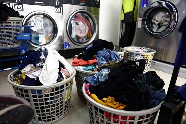 Laundry baskets filled with dirty clothes are lined up inside a laundromat — 스톡 사진