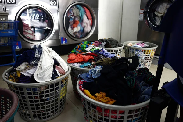 Cesti di lavanderia pieni di vestiti sporchi sono allineati all'interno di una lavanderia a gettoni — Foto Stock