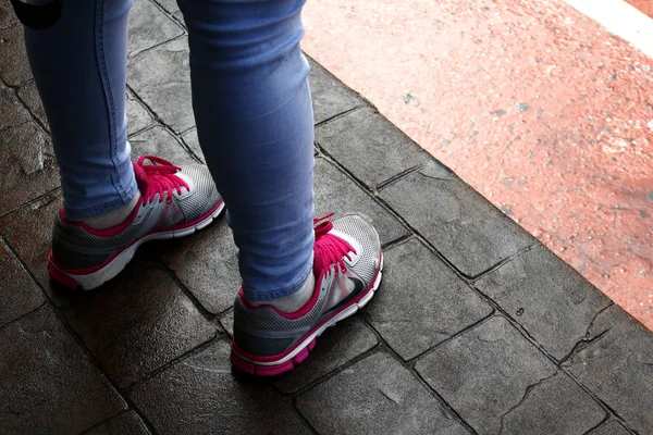 Женщина в разноцветных кроссовках и узких джинсах стоит на бетонном полу . — стоковое фото
