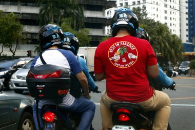 Bir motosiklet taksisinin yolcuları ve şoförleri kavşakta trafik lambasının yeşile dönmesini bekliyorlar.