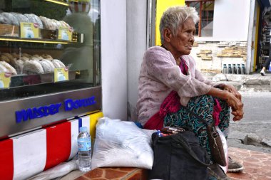 Yaşlı Filipinli kadın kaldırımda oturur ve insanların ona yemek ya da sadaka vermesi için yalvarır.