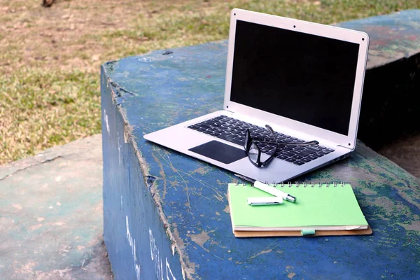 Ordenador portátil, anteojos, portátil y bolígrafo en un parque al aire libre —  Fotos de Stock
